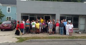 LArche Long Island board and commuinty group gather in front of the future community center and office. The blue building on the left is the home they plan to open in 2016. Photo provided